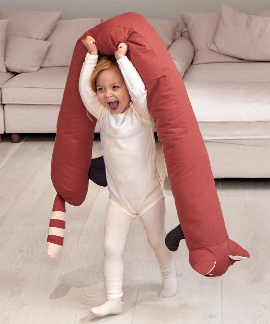 A child holding the Roommate red panda long cushion above the head while walking