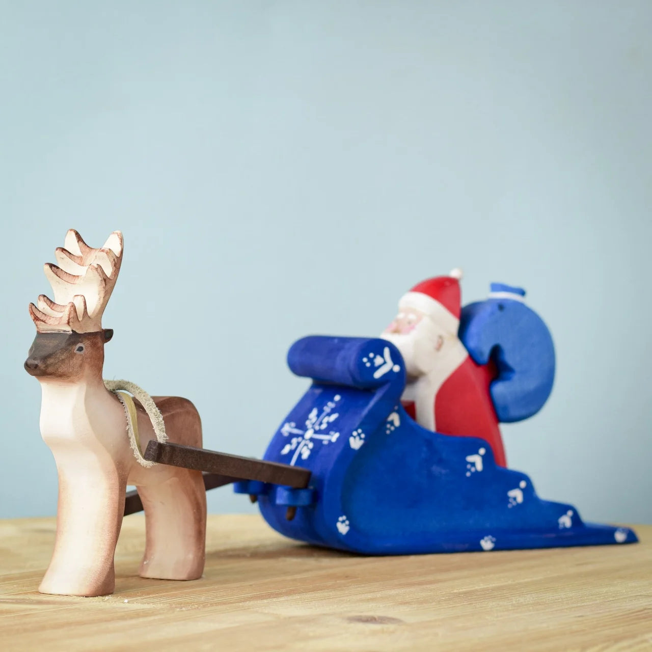 Bumbu Santa sitting in the back of the Snow Sleigh with a blue wooden sack on his back, and a Reindeer attached to the reins of the sleigh