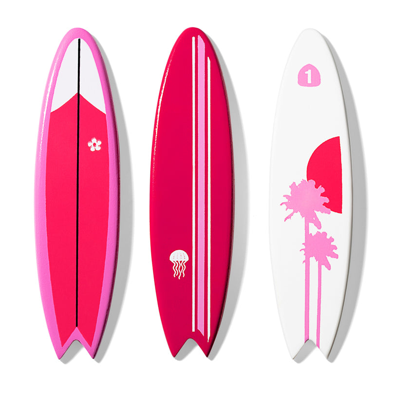 Three wooden toy Candylab surfboards with unique pink and white designs. One has a palm tree design