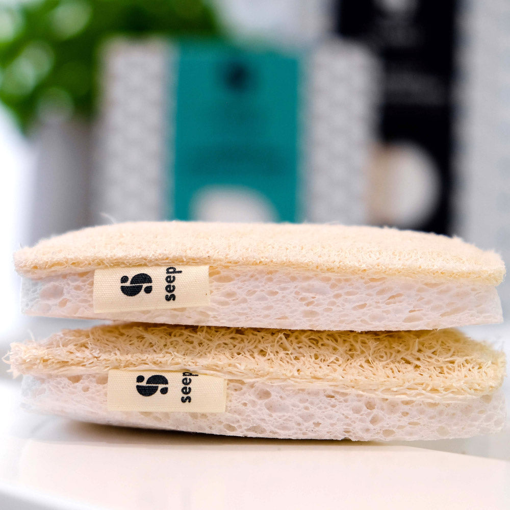 Close up of 2 Seep natural cellulose loofah sponges stacked on a white kitchen sink