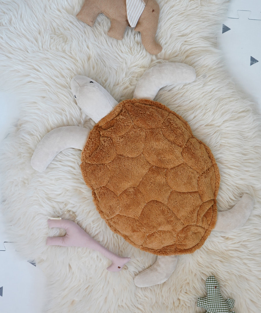 Senger Cuddly Rust Turtle - Small organic heatable soft toy on a fluffy white rug surrounded by other soft toys.