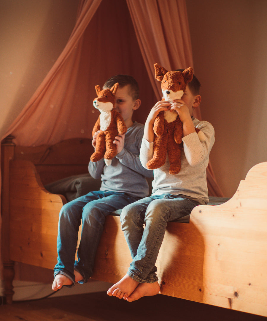 Two children sitting on as wooden bed holding up Senger Floppy Foxes in front of their faces.