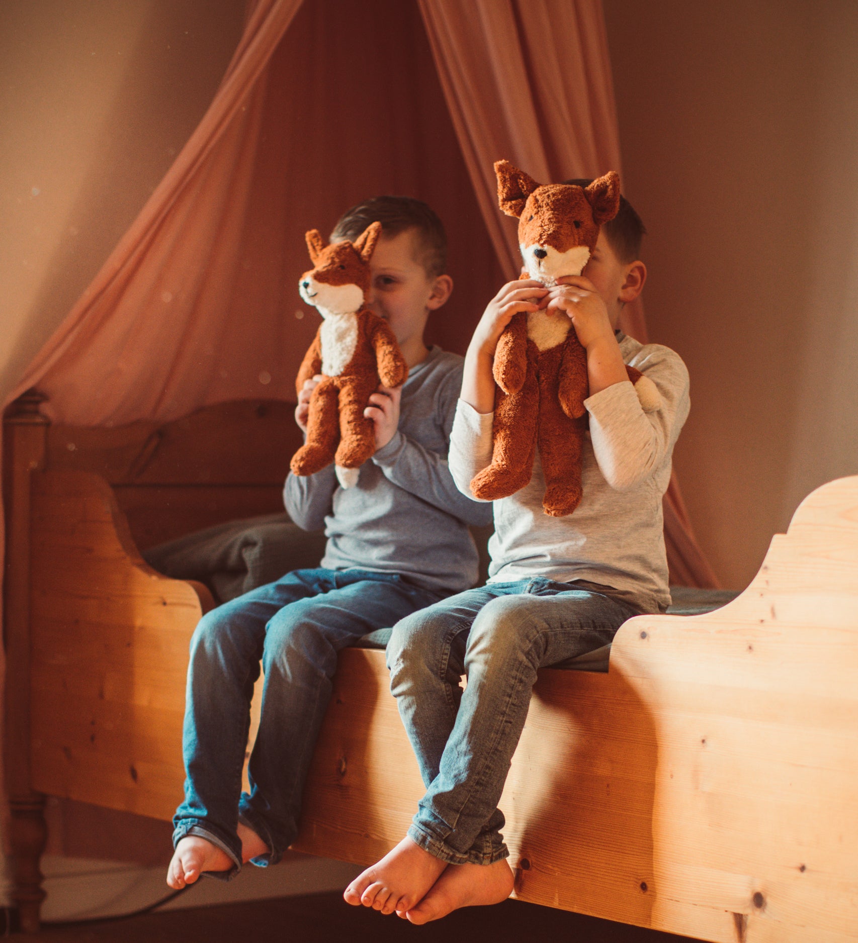 Two children sitting on as wooden bed holding up Senger Floppy Foxes in front of their faces.