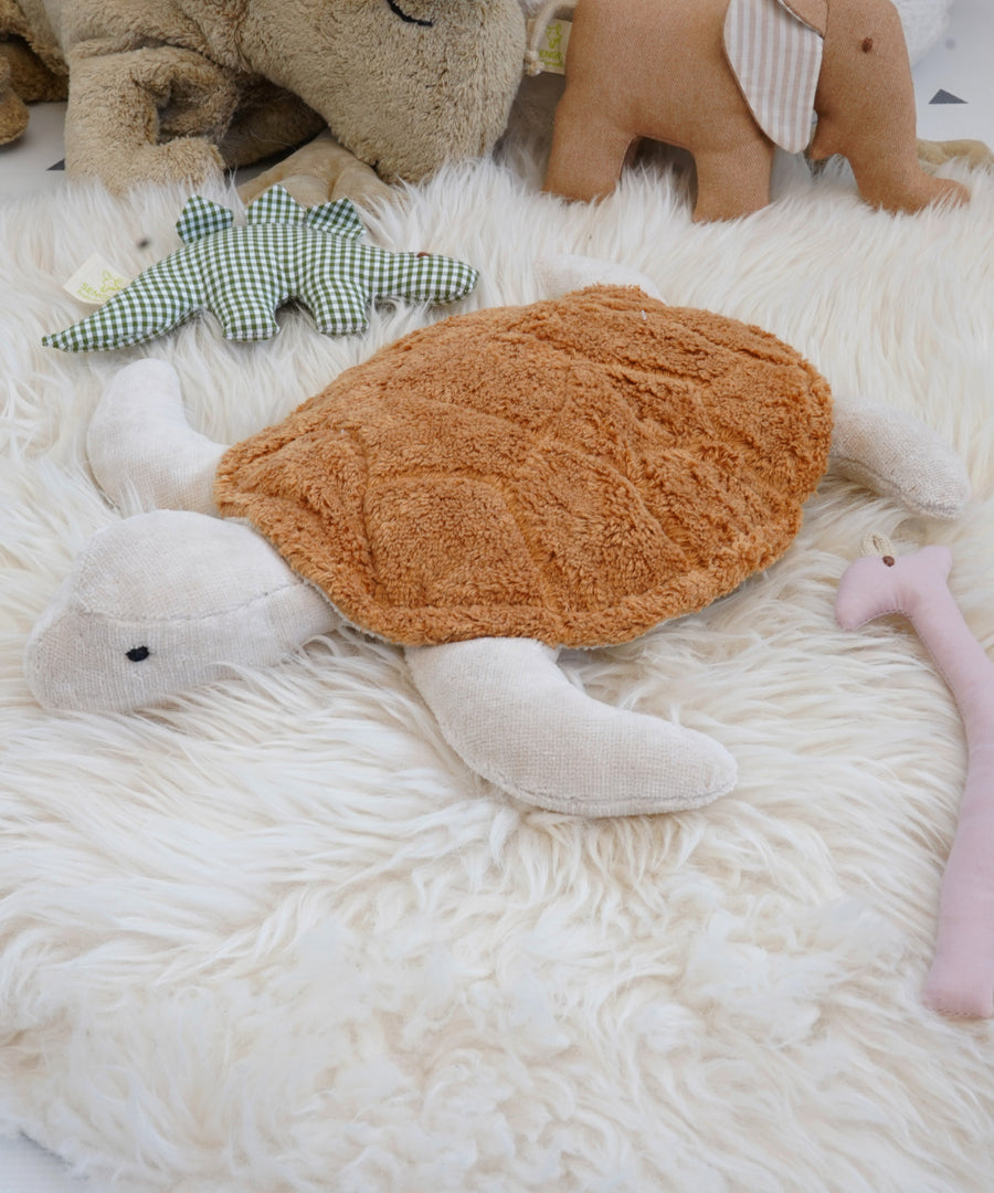 Senger Cuddly Rust Turtle - Small organic heatable soft toy on a white fluffy rug surrounded with other stuffed toys. 