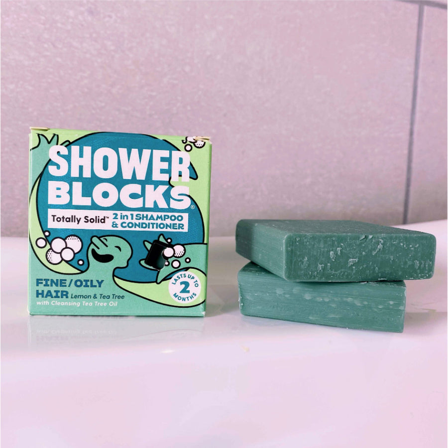 Stack of Shower Blocks eco-friendly lemon and tea tree solid shampoo and conditioner bars on the side of a bath