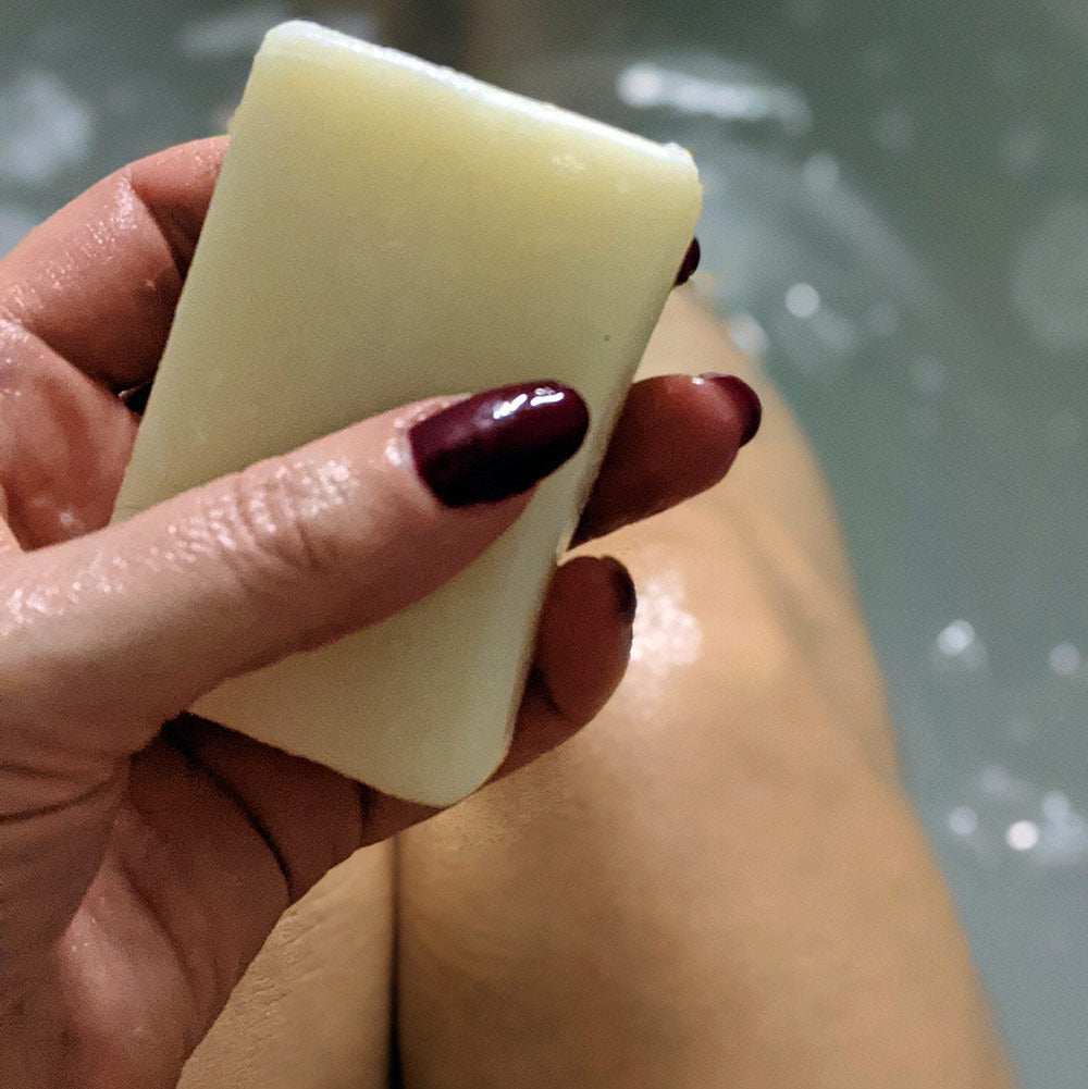 A person with dark red nail polish holding a shower blocks solid gel bar