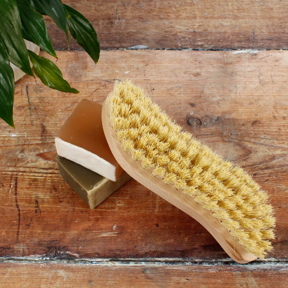 A Slice of Green beech wood scrubbing brush upturned on top of some soap bars on a wooden floor