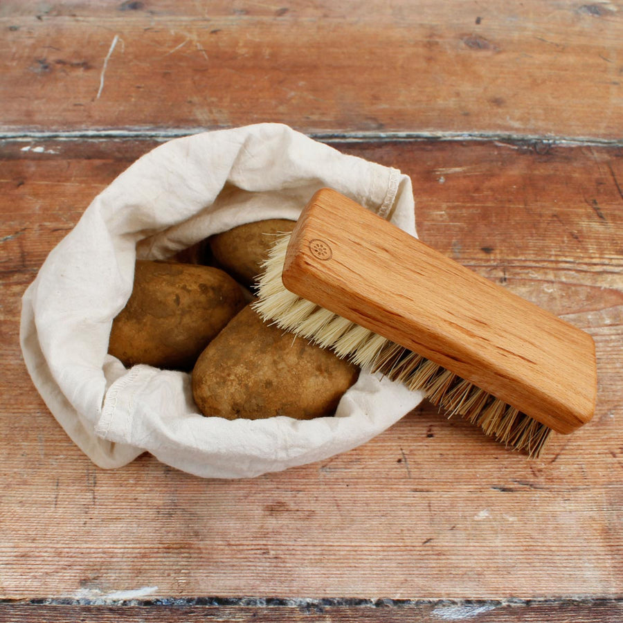 A Slice of Green plastic-free wooden vegetable brush on a white background next to a pile of potatoes