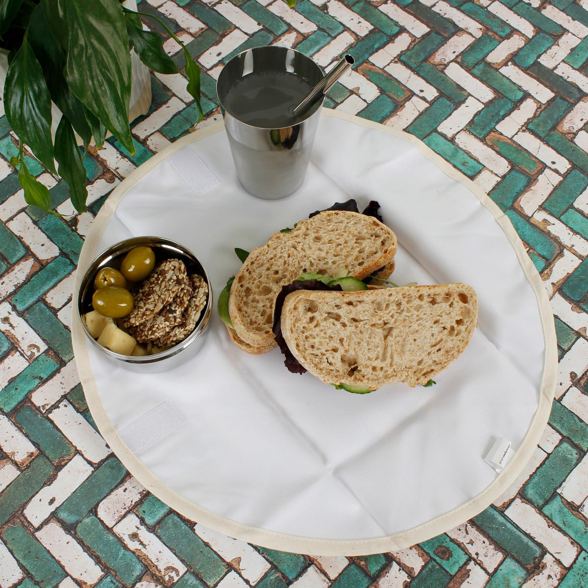 A Slice of Green organic cotton food wrap on some green and white tiles with a sandwich