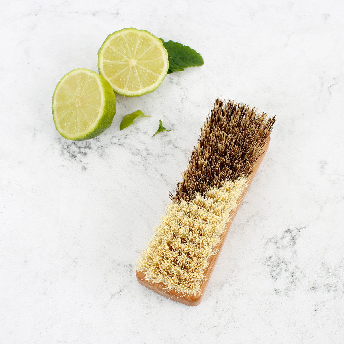 A Slice of Green plastic-free vegetable brush upturned on a white background next to a sliced lime