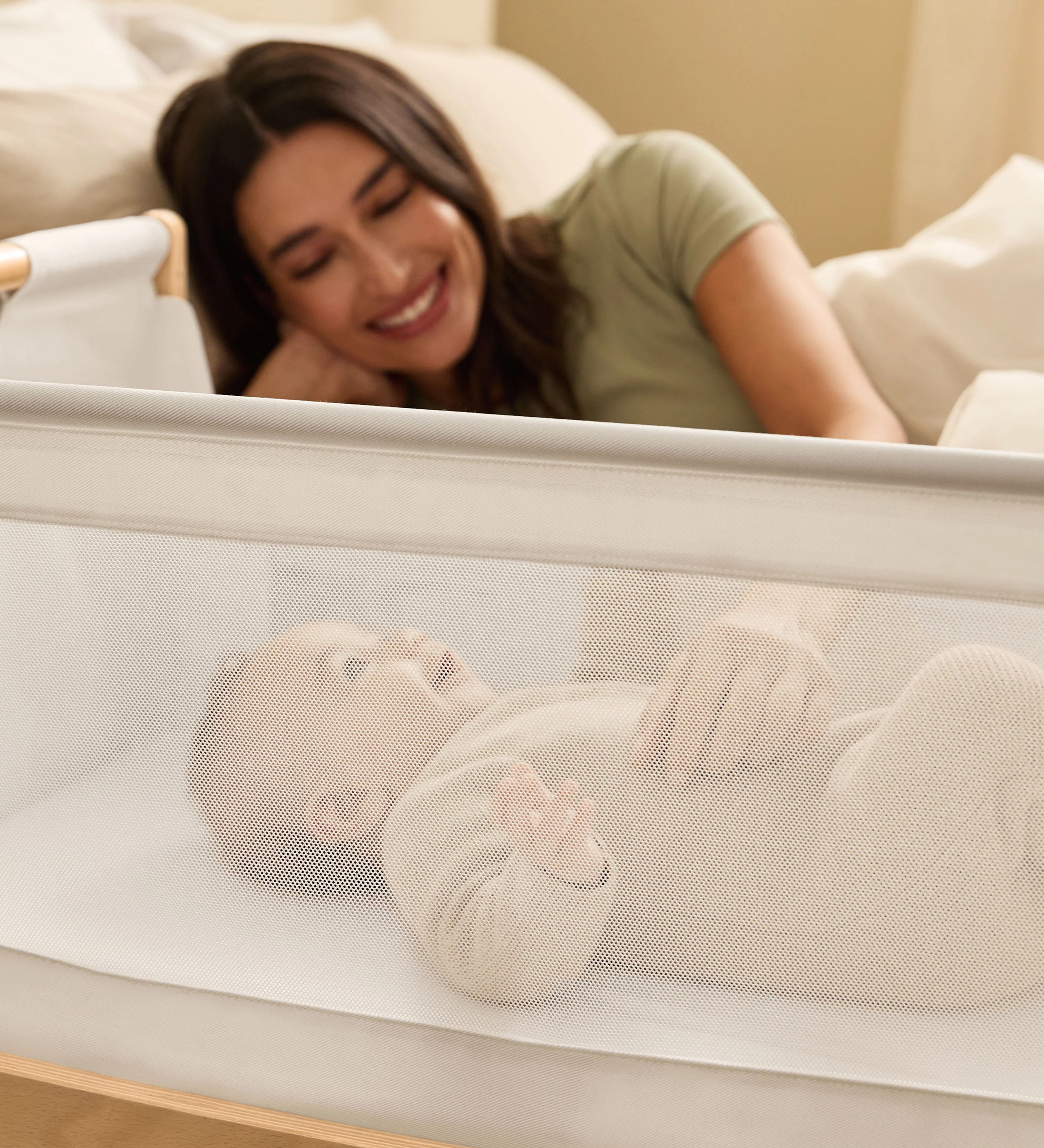 A woman watching over her baby from bed, with the SnuzPod5 close to her bedside.