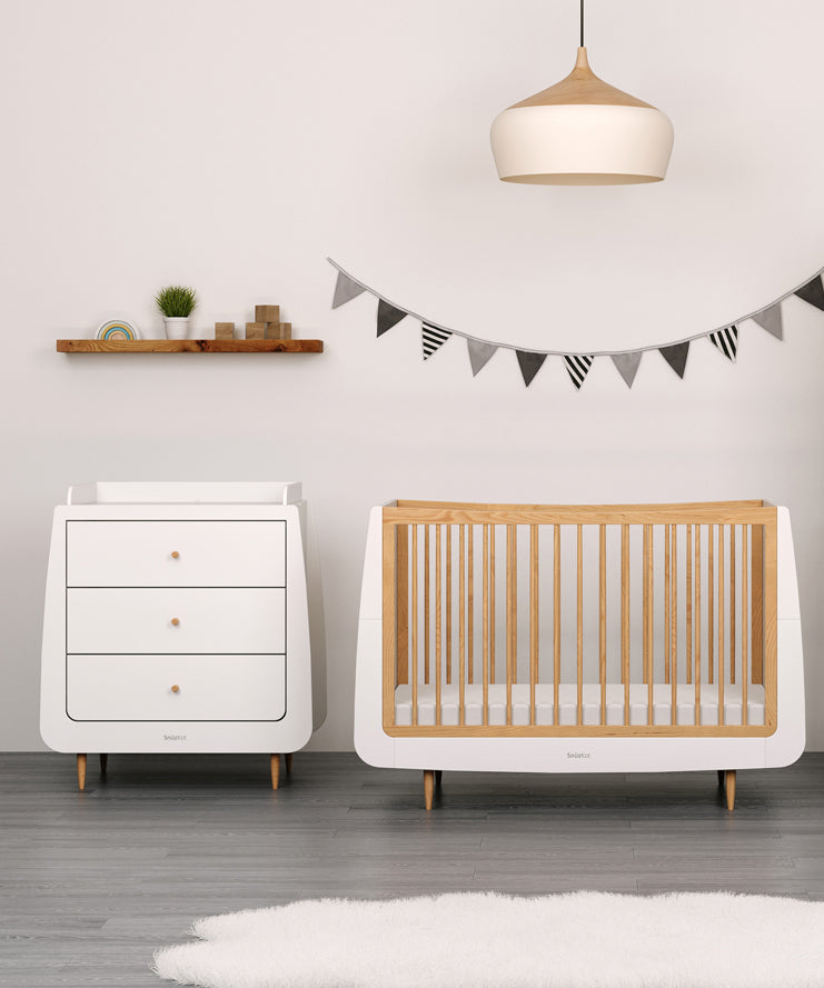 A natural SnuzKot changing unit pictured next to a matching cotbed