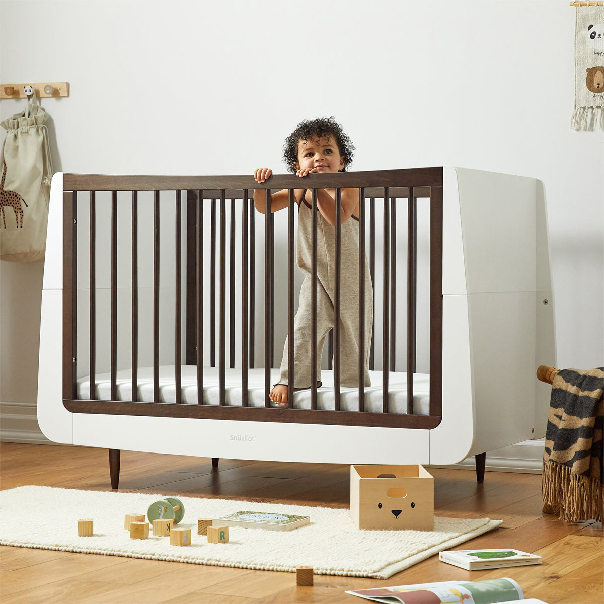 A SnuzKot Cot bed in ebony pictured in a nursery. A child with curly hair can be seen standing up in the cot holding onto the side