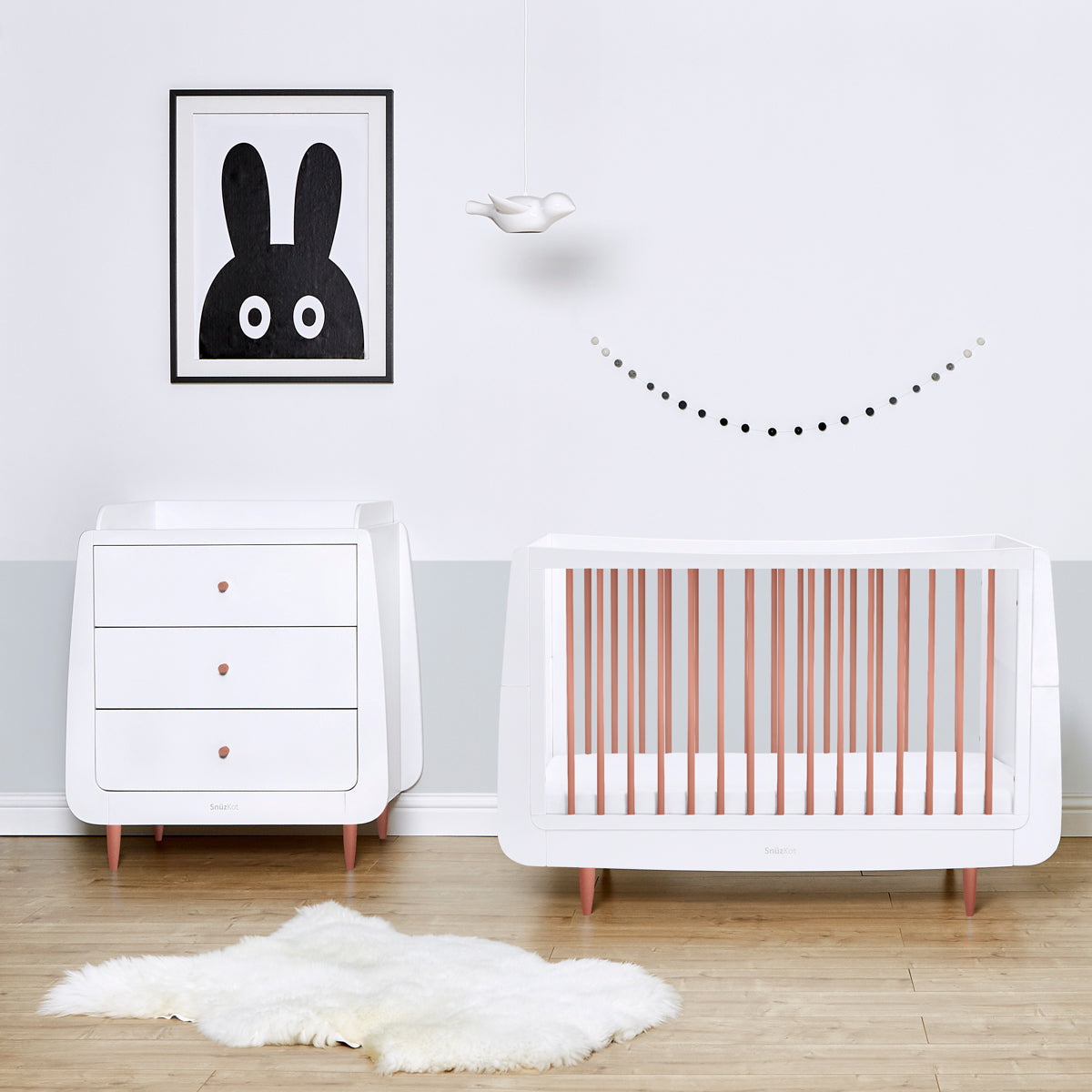 A rose gold SnuzKot pictured in a nursery pictured next to a changing unit