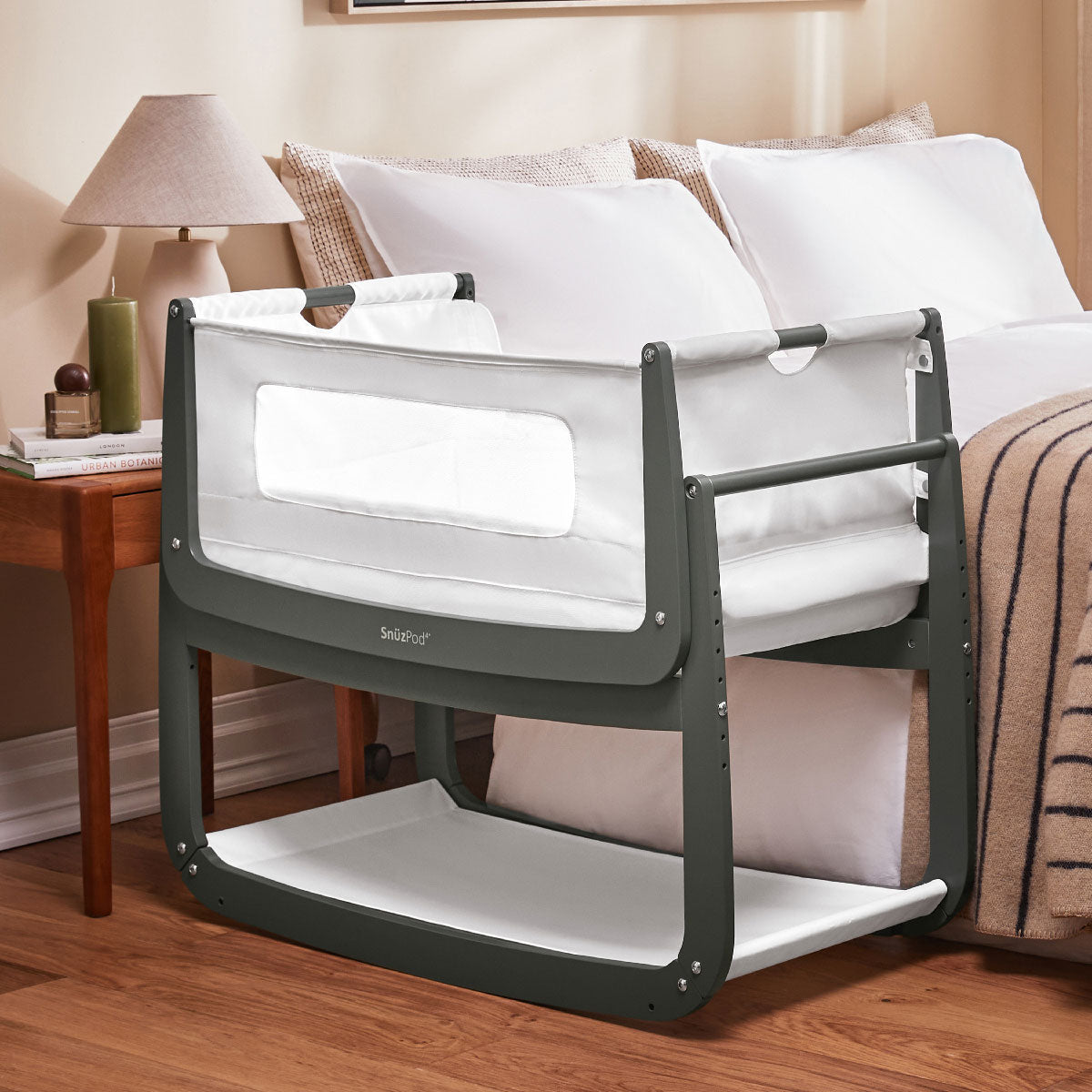 A sage green coloured SnuzPod 4 placed beside a bed