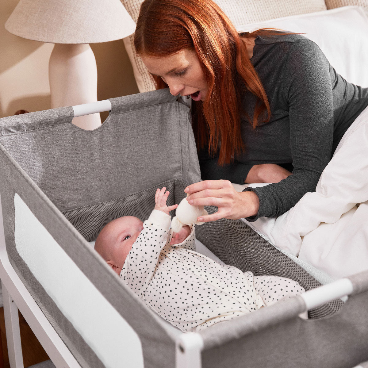 An adult is seen holding up a soft toy above a baby that is seen lying down in the dusk coloured SnuzPod 4. The baby is reaching for the toy