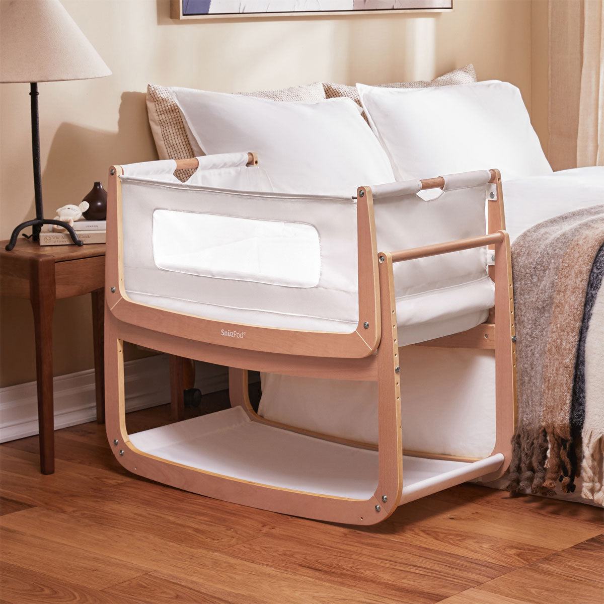 A SnuzPod 4 bedside crib in natural pictured placed next to a bed