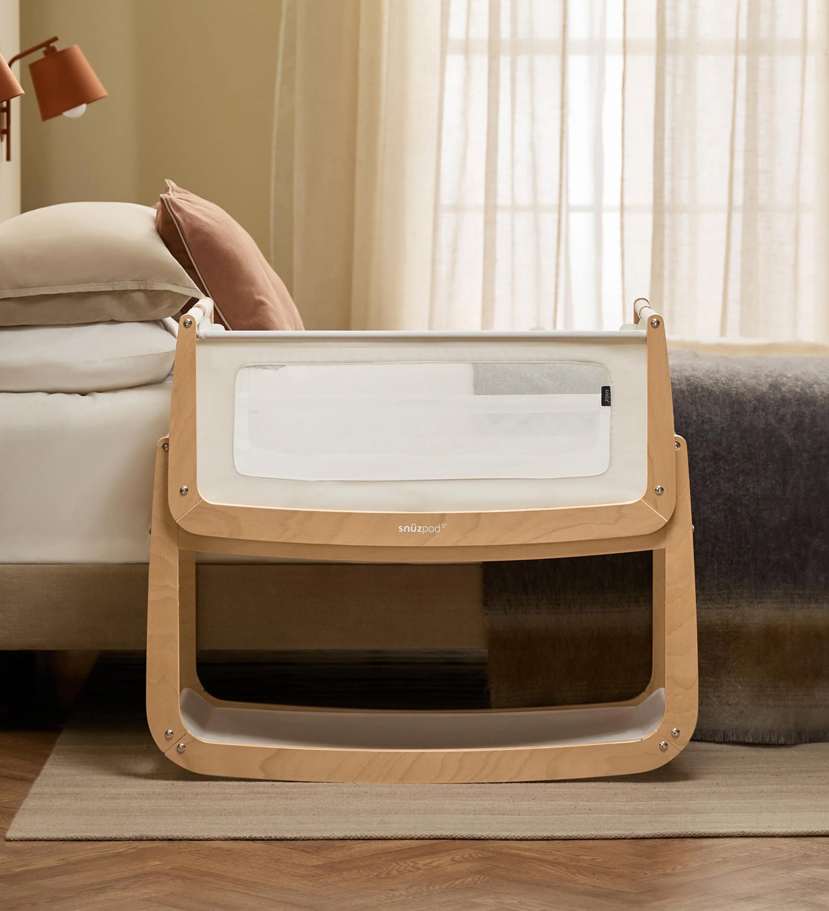 The SnuzPod 5 bedside baby crib with a lovely natural wooden frame, next to an adult's bed in a beautifully decorated bedroom.