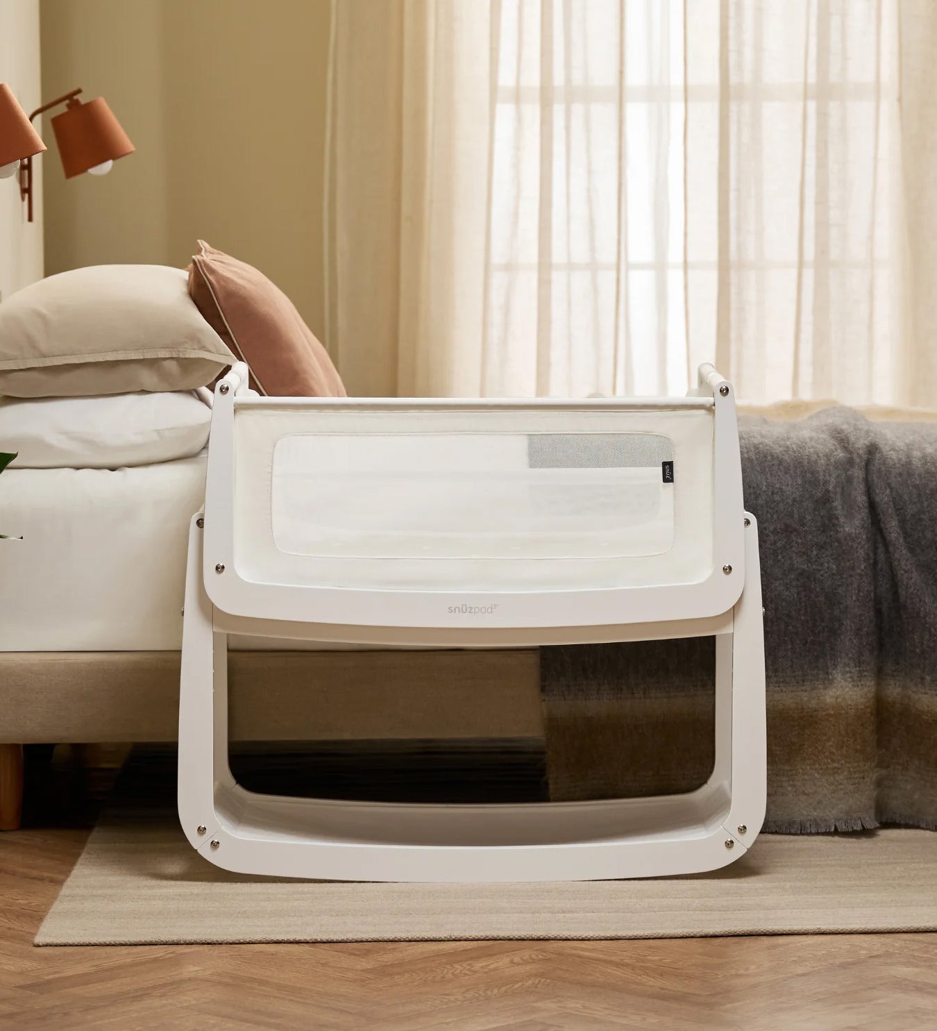 The SnuzPod 5 bedside baby crib with a lovely white wooden frame, next to an adult's bed in a beautifully decorated bedroom.