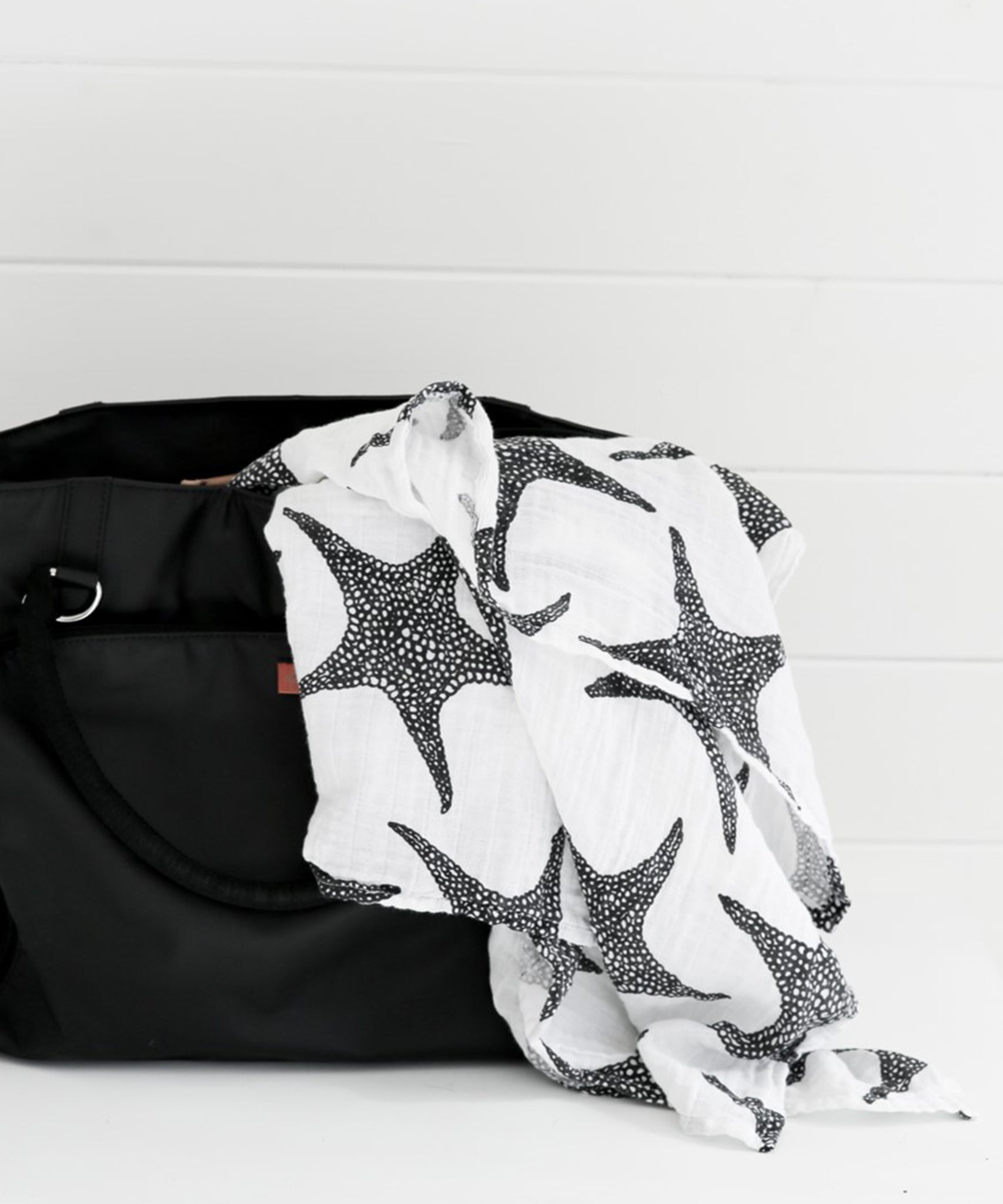 A child in a baby bouncing chair looking at the XL Starfish Muslin cloth which is laid out on the side of a bath tub