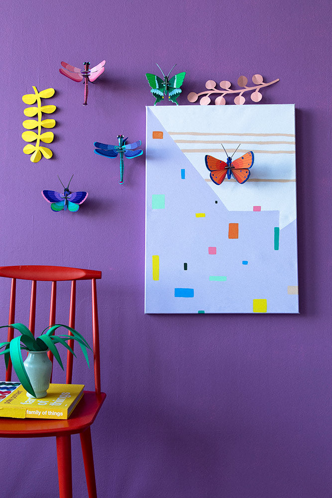 Stuio Roof insects mounted on a purple wall with a red chair in front and a plant and books