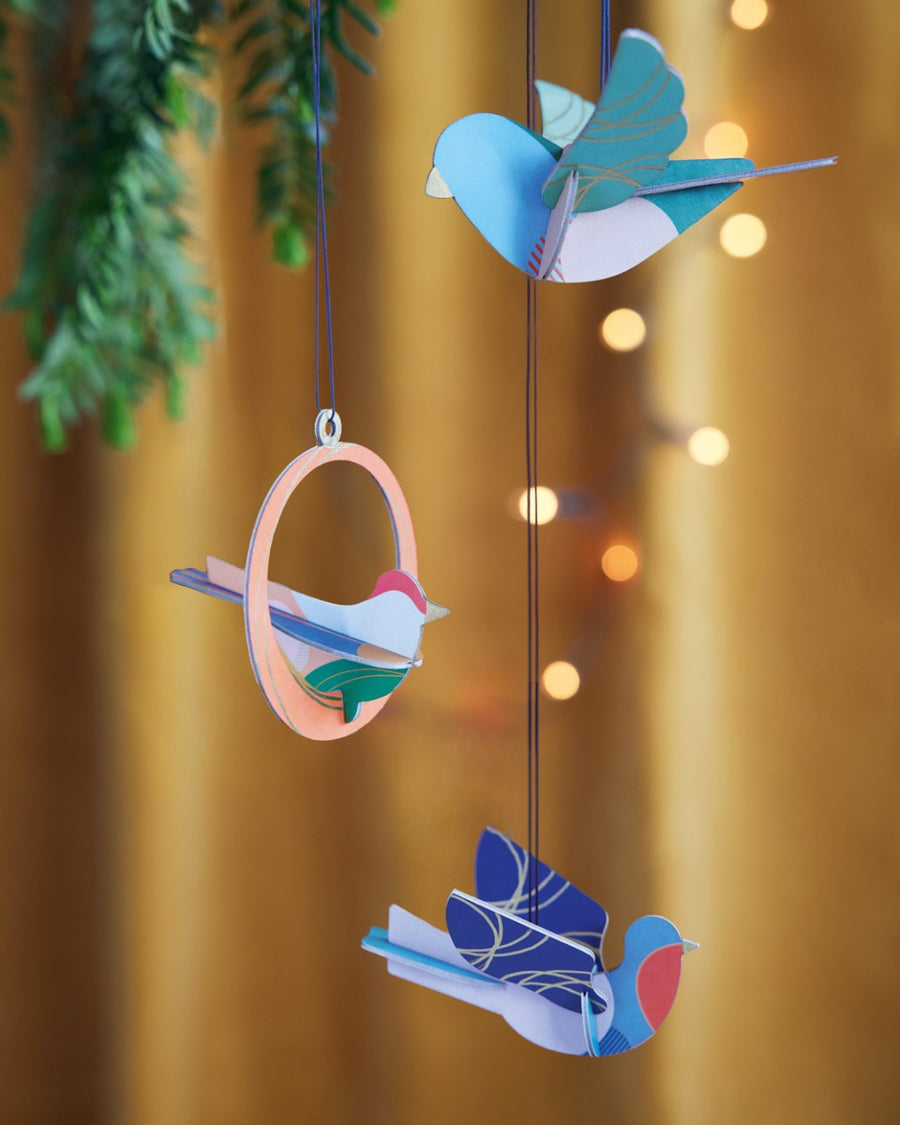 Close up of the Studio Roof plastic-free Calling Birds decorations hanging from a Christmas tree in front of an orange background