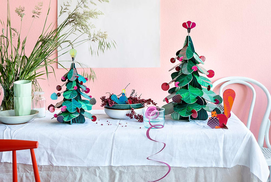 Studio Roof Large cardboard Christmas Tree & cardboard Squirrel Decor in the front and a smaller Christmas Tree with a cardboard peacock in a fruit bowl on a table