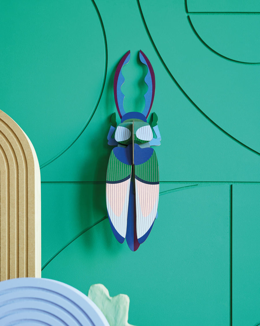 Studio roof slotting card antler beetle figure attached to a green patterned wall