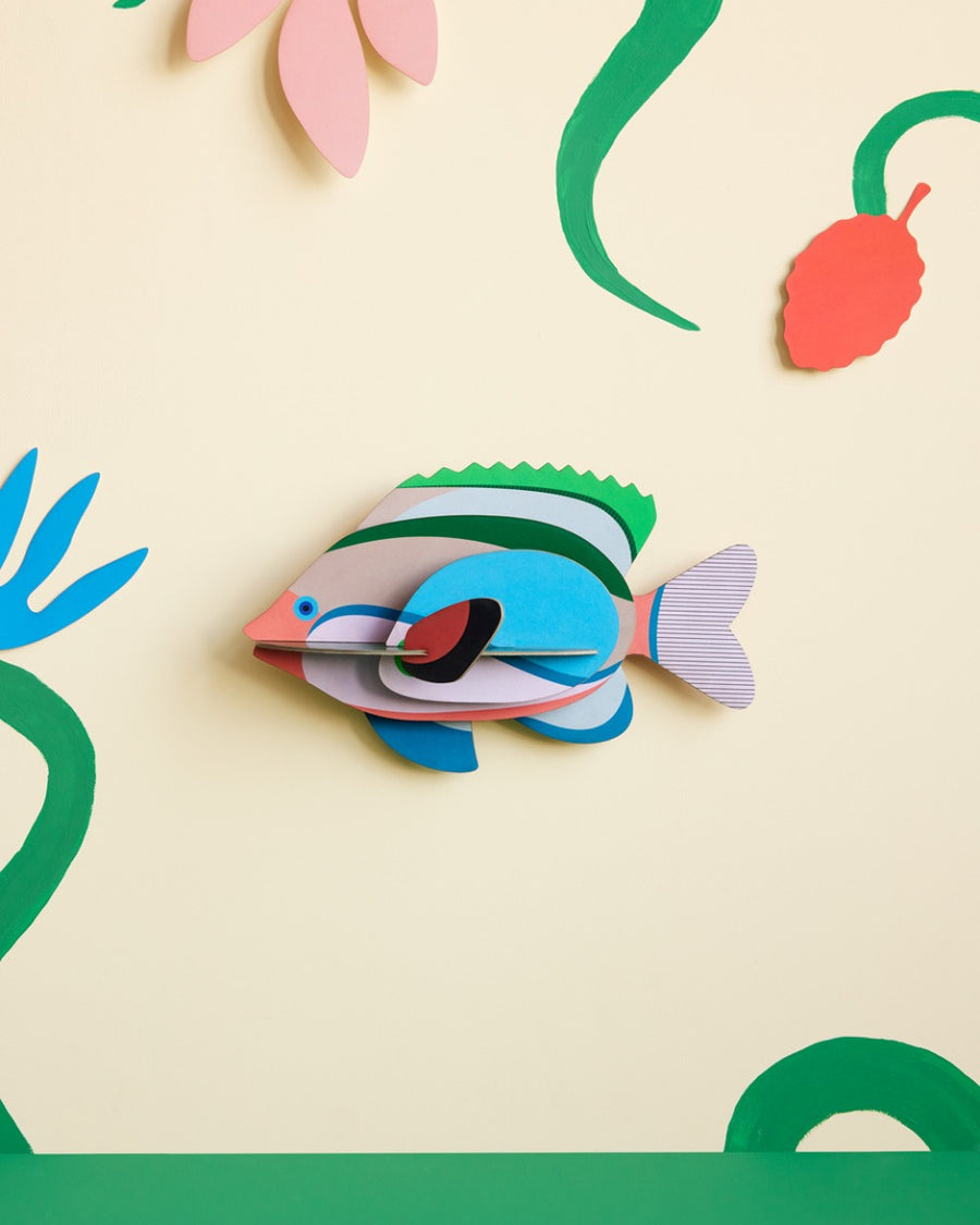 Studio Roof plastic-free Fairy Wrasse card wall decoration on a beige wall next to some green painted plants