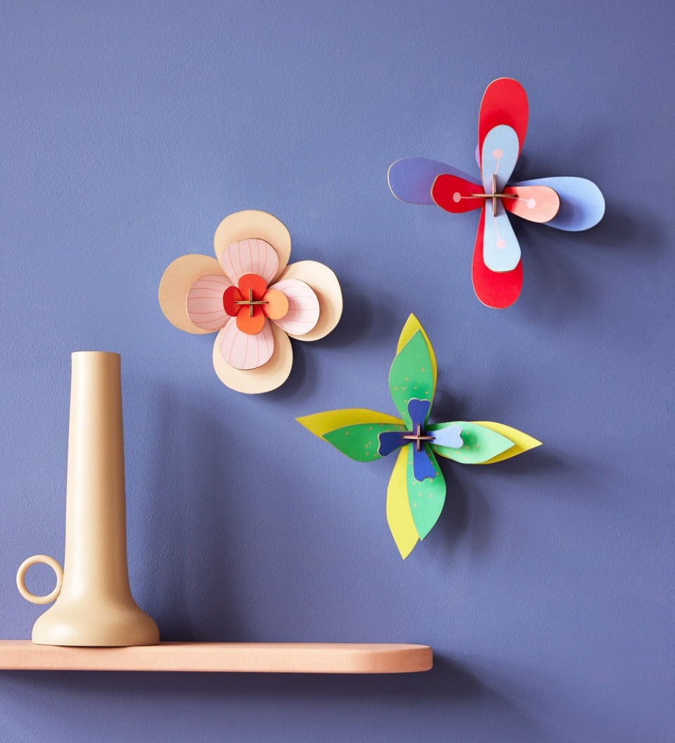 3 Studio Roof craft flowers hung on a purple wall next to a beige shelf and candle holder