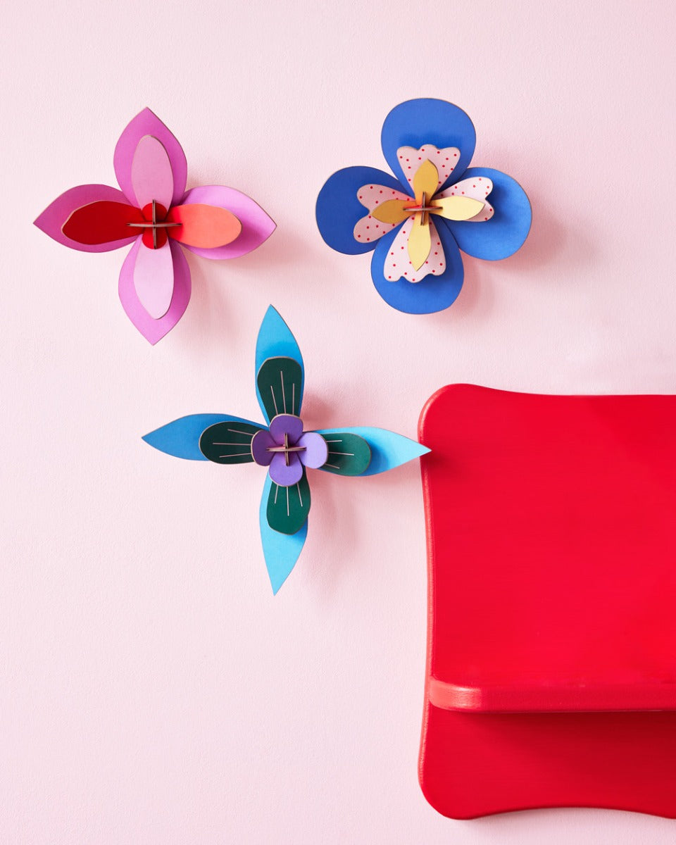 3 Studio Roof plastic-free craft flowers hung on a pink wall next to a red painted shelf