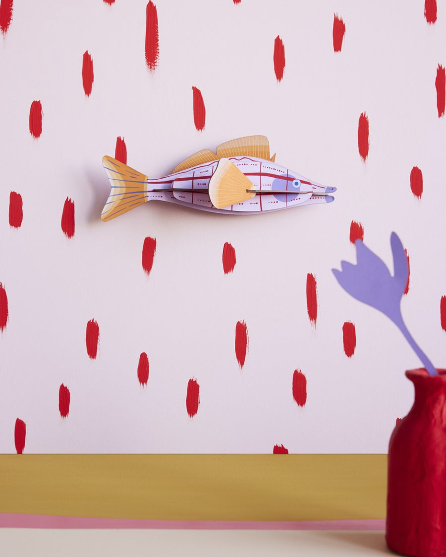 Studio Roof plastic-free card fish wall decoration hanging on a pink and red wall next to a red potted plant