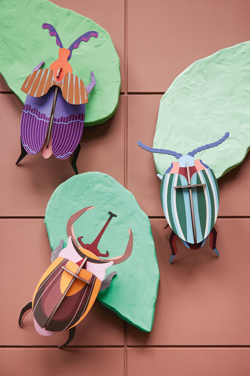 3 Studio roof slotting craft model beetles climbing on some green model leaves on a brown background