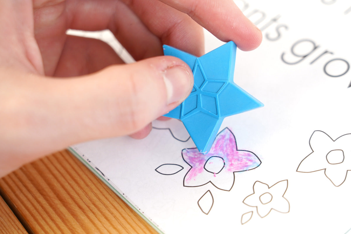 Close up of a hand holding a blue Crayon Bug festive crayon over a colouring book picture