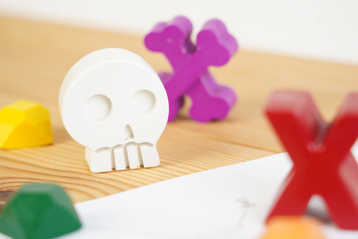 Close up of a crayon bug white crayon skull on a wooden work top next to some crayon bug pirate treasure crayons