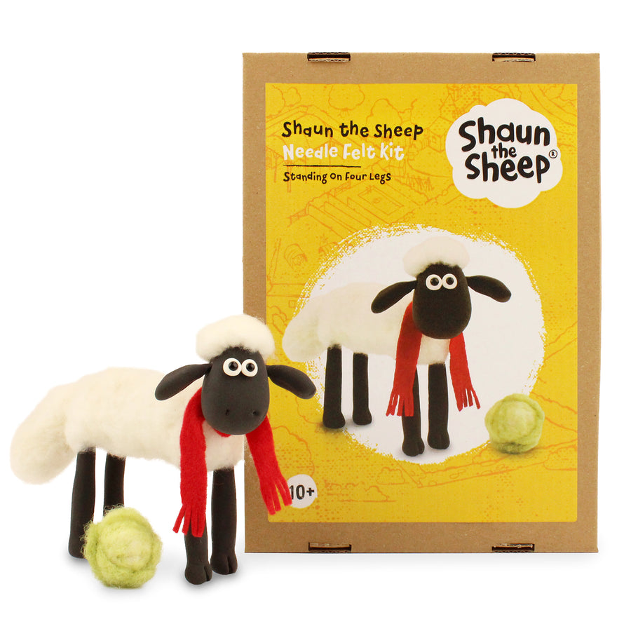 The Makerss Shaun The Sheep On Four Legs Needle Felt character with a fluffy felted body, red scarf and green lettuce, next to the craft box on a white background