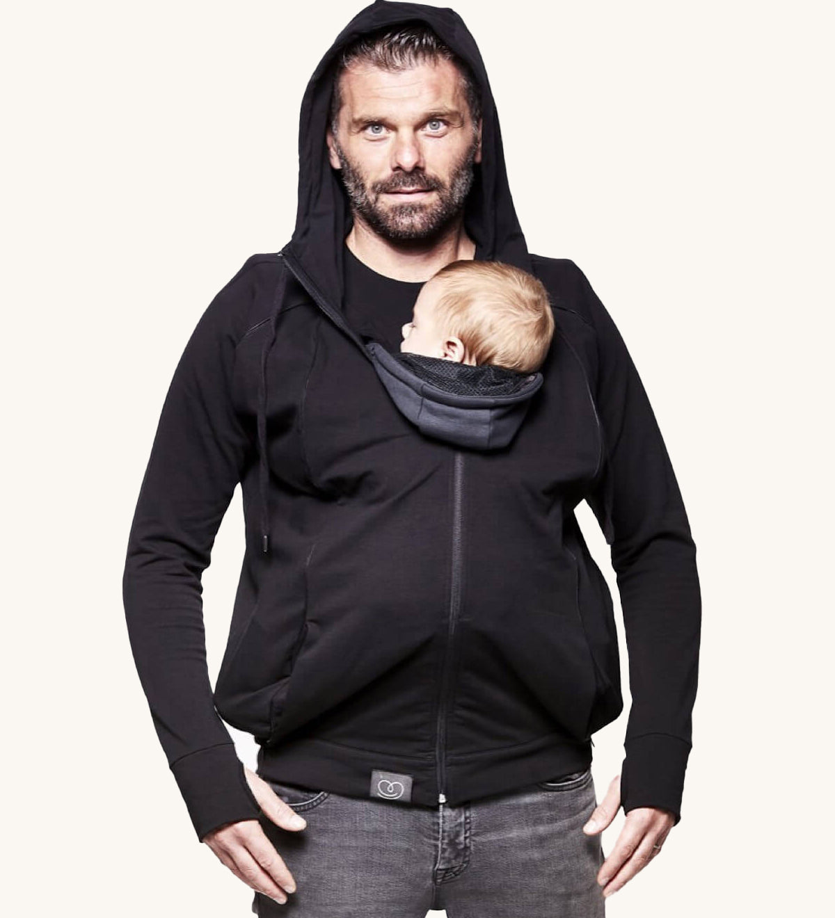 An adult wearing the Love Radius Parent Hoodie in Black, whilst carrying a child inside, on a cream background