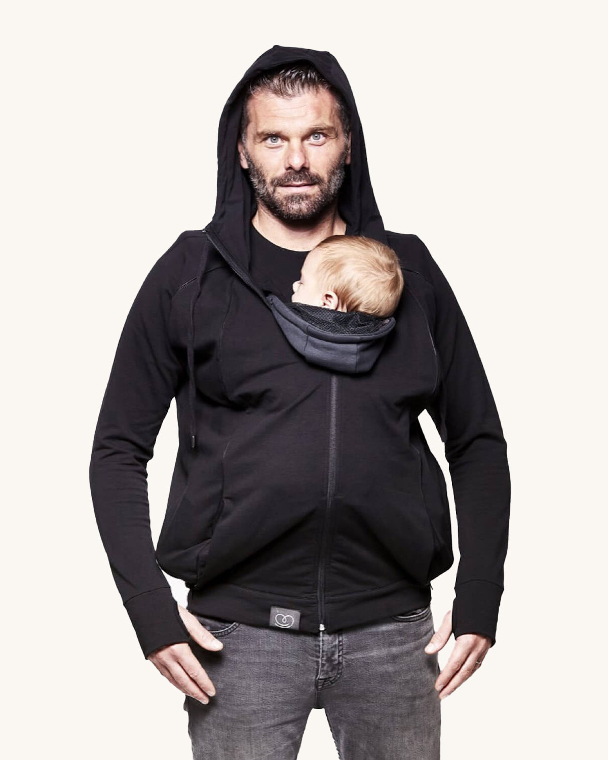 An adult wearing the Love Radius Parent Hoodie in Black, whilst carrying a child inside, on a cream background