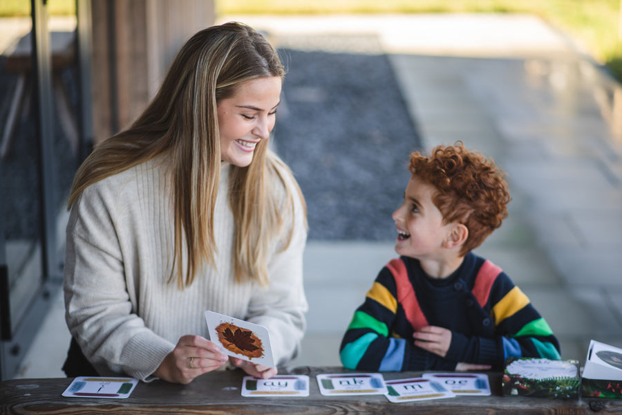 An adult sitting next to a child with a The Phive Enchanting Learning Phonics & Storytelling Card Set laid out in front of them