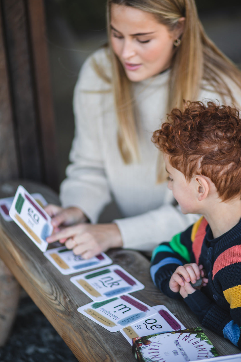 An adult sitting next to a child with a The Phive Enchanting Learning Phonics & Storytelling Card Set laid out in front of them