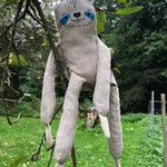 Tobe children's plush hemp sloth figure sitting on a tree branch in front of a field