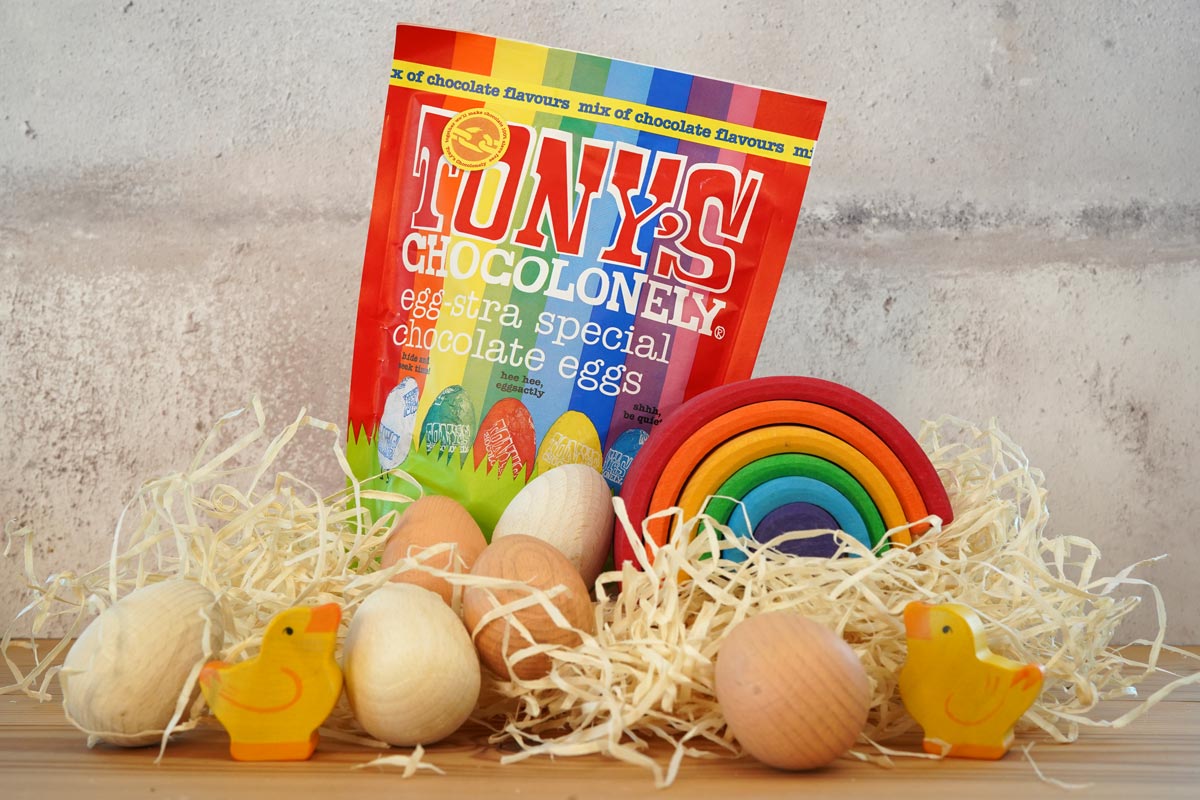 Tonys chocolonely fairtrade mini chocolate easter eggs in the mixed flavours pack on a pile of straw next to a grimms rainbow and some wooden eggs