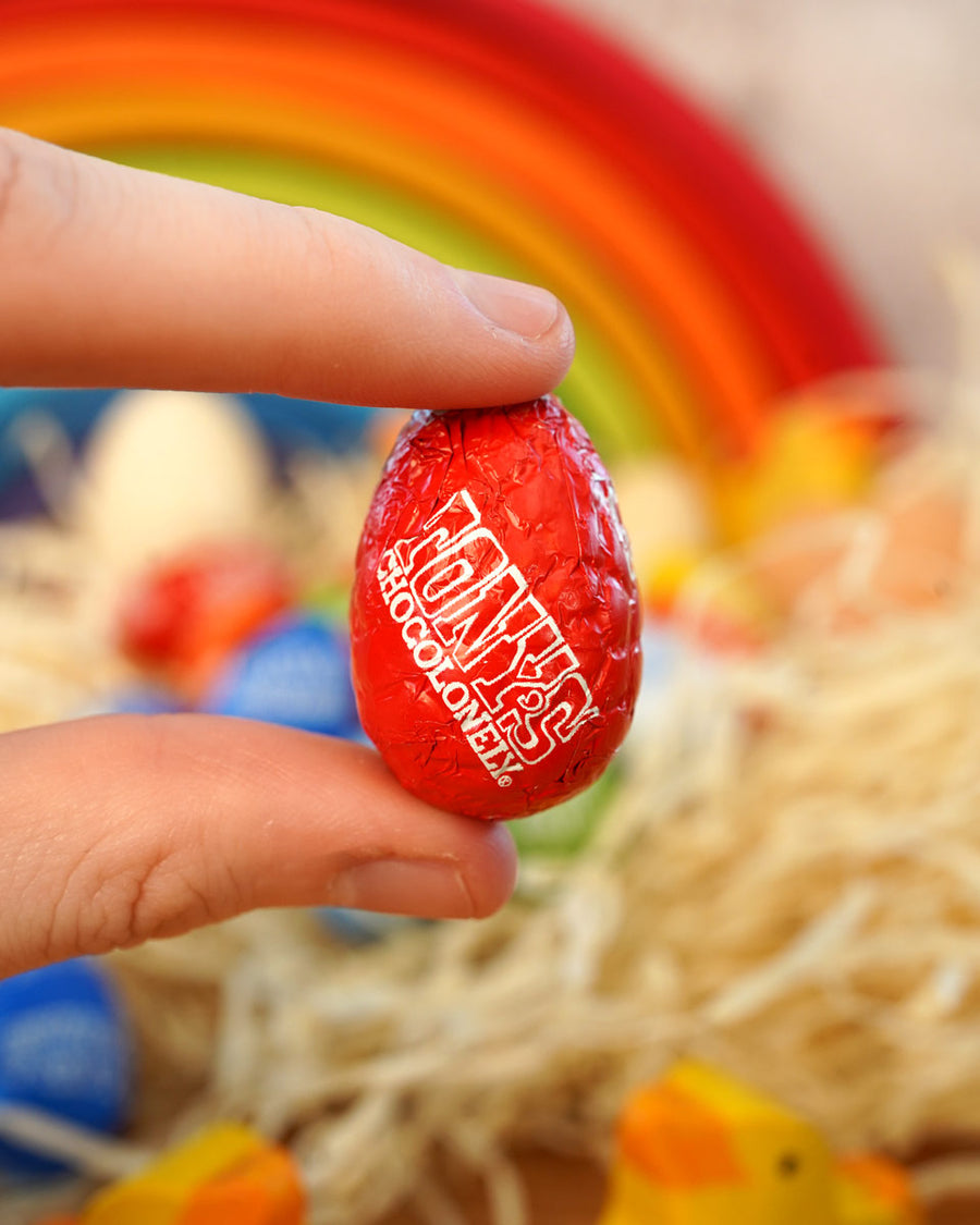 Close up of a hand holding a Tonys Chocolonely eco-friendly fairtrade mini chocolate easter egg in front of a grimms rainbow