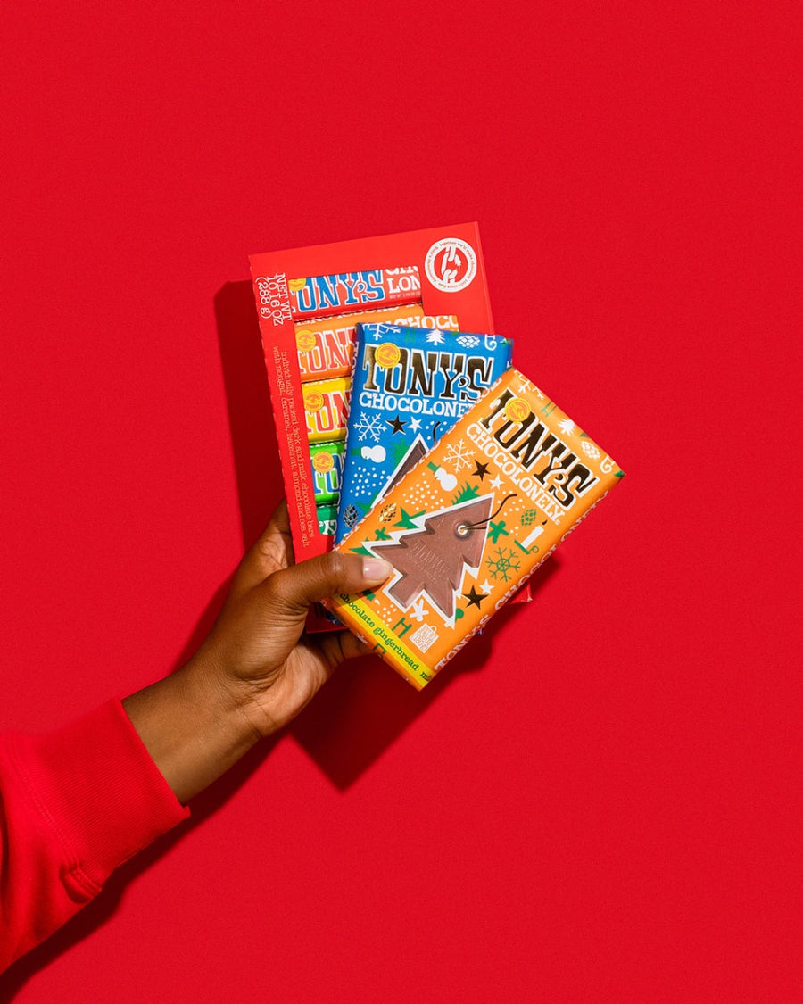 Close up of hand holding an assortment of Tony's Fairtrade Christmas chocolate bars in front of a red background