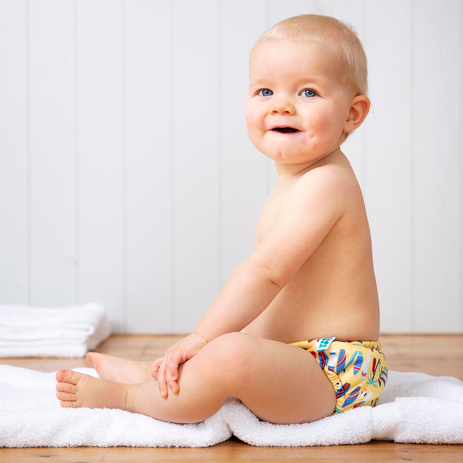 Toddler sat on a white towel wearing the Totsbots surfs up eco-friendly reusable baby swim pants 