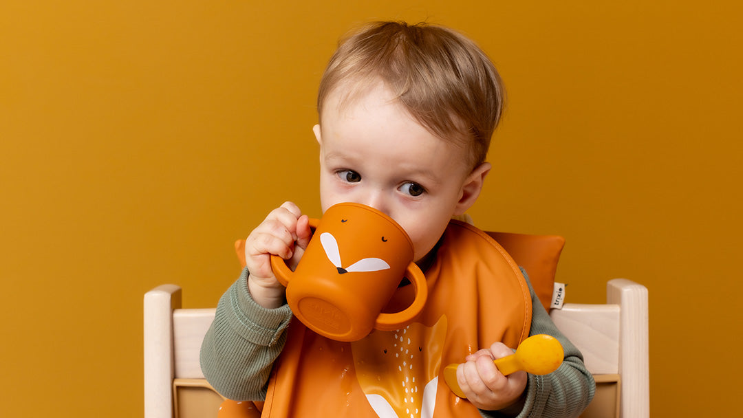 A toddler drinking from a trixie fox sippy cup, with matching bib and cutlery.