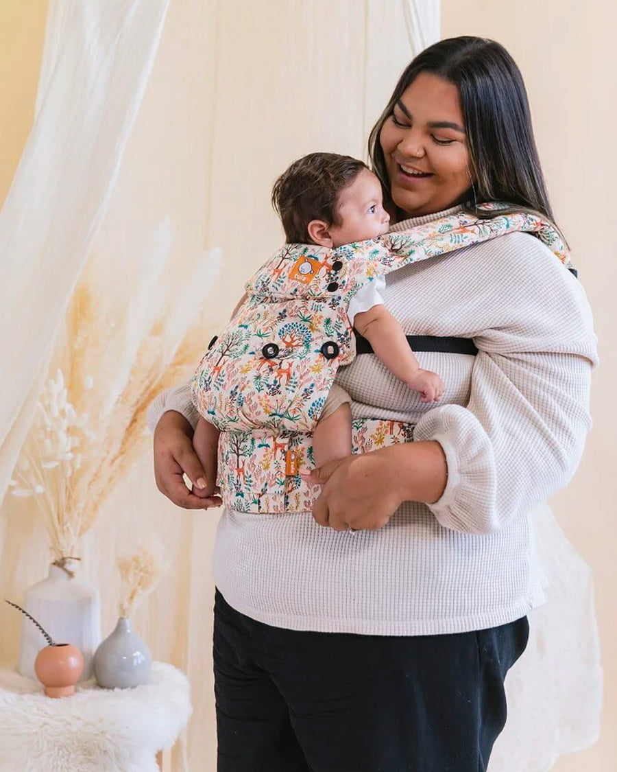 Woman stood carrying a baby in the Tula white woodland print explore baby carrier