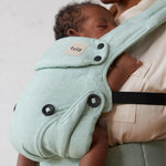 A baby is fast asleep in the Explore Eucalyptus Carrier. Parent is gently touching the babies feet and looking down at the baby