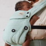 A baby is fast asleep in the Explore Eucalyptus Carrier. Parent is gently touching the babies feet and looking down at the baby