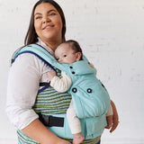 Woman stood with a baby inside a Tula explore baby carrier in the light blue robin colour